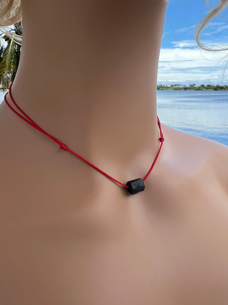 Puede incluir: Un collar sencillo con un colgante de piedra negra en un cord&oacute;n rojo.