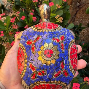 Può includere: Una statuetta decorativa a forma di tartaruga con un guscio a mosaico realizzato con piccoli pezzi intarsiati di pietra blu e rossa. Il guscio è arricchito da motivi floreali in metallo dorato e da testa, coda e quattro zampe color argento.