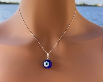 May include: A silver chain necklace with a blue evil eye pendant. The pendant is round and has a white center.