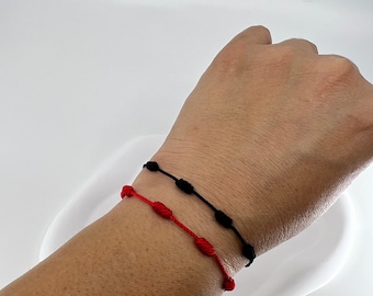 May include: Two friendship bracelets, one red and one black, with knotted beads, worn on a wrist.