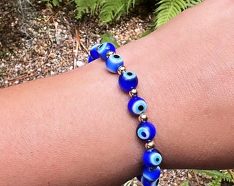 May include: A blue and gold evil eye bracelet with multiple beads. The bracelet is on a person's wrist.
