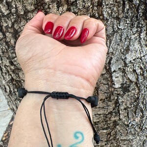 May include: A black cord bracelet with black beads on the ends. The bracelet is tied with a knot in the center.