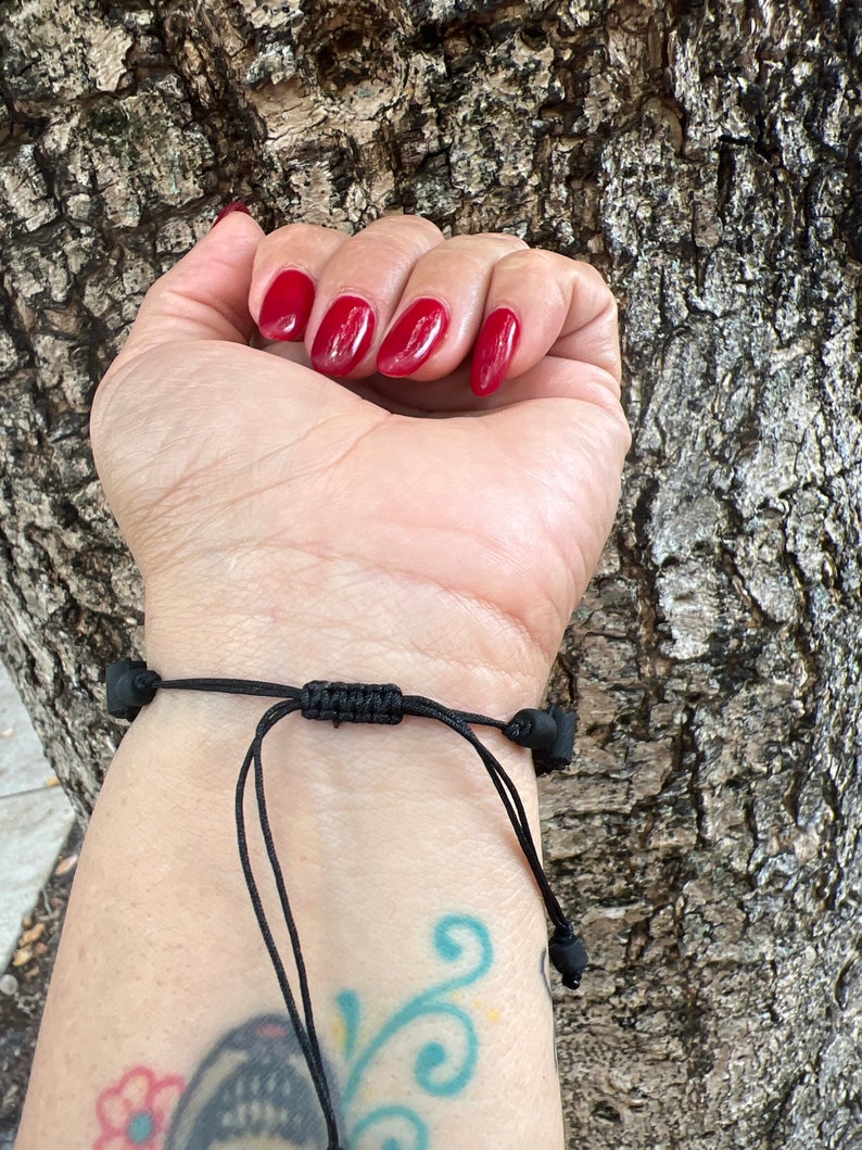 May include: A black cord bracelet with black beads on the ends. The bracelet is tied with a knot in the center.