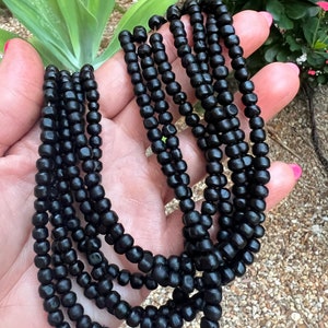 May include: A black wooden bead necklace with multiple strands. The necklace is made of small, round beads that are strung together in a simple pattern.