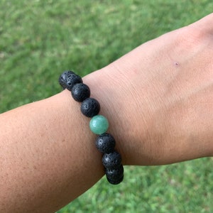 May include: A black lava rock and green gemstone beaded bracelet. The bracelet is on a person's wrist.
