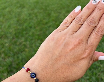 Puede incluir: Un brazalete de cuerda azul con una cuenta roja, una cuenta negra y un dije de ojo turco azul.
