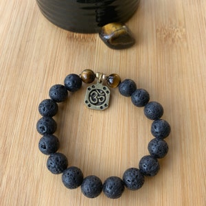 May include: A black lava rock bracelet with a gold Om charm and tiger's eye beads.