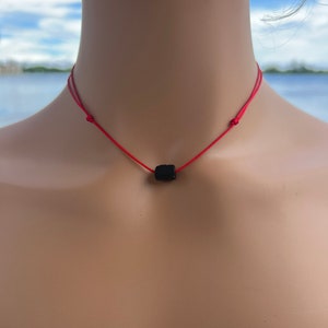 Puede incluir: Un collar de cuerda roja con una cuenta de lava negra.
