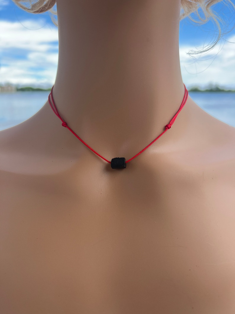Puede incluir: Un collar de cuerda roja con una cuenta de lava negra.