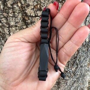 May include: A black beaded bracelet with a black rectangular charm. The bracelet is made of small, round beads and has a simple, minimalist design.