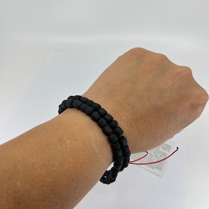 May include: A black beaded bracelet with a red string tie closure. The bracelet is worn on a person's wrist.