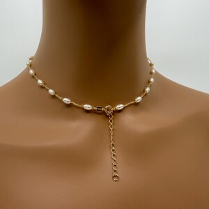May include: A delicate necklace featuring small, oval-shaped pearls strung along a gold-colored chain. The necklace has a simple design with a clasp and an adjustable chain. The pearls are a creamy white color.