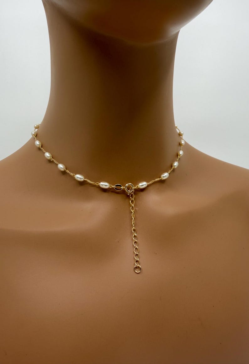 May include: A delicate necklace featuring small, oval-shaped pearls strung along a gold-colored chain. The necklace has a simple design with a clasp and an adjustable chain. The pearls are a creamy white color.