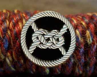 Peut inclure: Une épingle en émail noir avec un motif de nœud de corde blanc. L'épingle est ronde et a une bordure blanche.