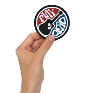 May include: A round, black, white, red, and blue embroidered patch with a guitar and the words "PLAY DEAD" in a circle.