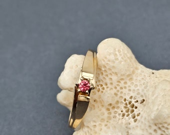 May include: A gold ring with a single pink gemstone set in the center.