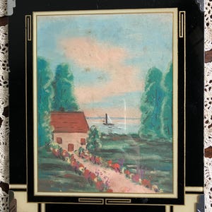 May include: A framed pastel artwork depicting a quaint cottage with a red roof, a path lined with flowers, and a sailboat on the water. The artwork is set within a black frame with silver corner accents and a cream-colored border.