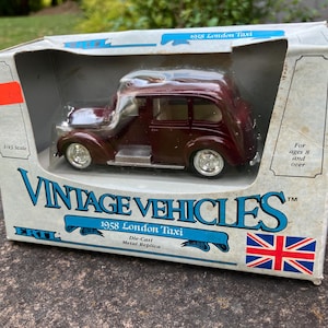 May include: A die-cast metal replica of a 1958 London Taxi in a display box. The burgundy-colored taxi is a 1/43 scale model. The box features the text "VINTAGE VEHICLES" and a Union Jack flag.
