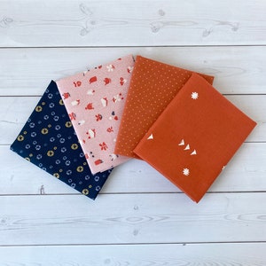 May include: Four fabric squares with different patterns. The top square is a light brown with small white dots. The second square is a light pink with a white and red pattern of houses, flowers, and watering cans. The third square is a dark blue with a white and yellow pattern of circles and stars. The bottom square is a dark orange with a white pattern of small flowers and triangles.