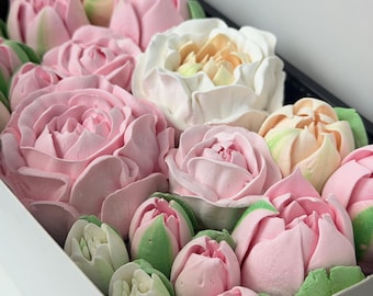 May include: A collection of edible flower-shaped confections arranged in a white box. The assortment features various shades of pink, white, and pale peach, with green accents on the base of the buds, resembling roses and tulips in full bloom.