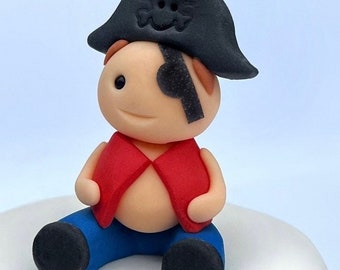 May include: A small, red and blue fondant figurine of a pirate with a black eyepatch and a black hat with a skull and crossbones design.