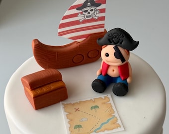 May include: A white iced cake decorated with a pirate theme. It features a small brown ship with a red and white striped sail, a pirate figurine, a treasure chest, and a treasure map.