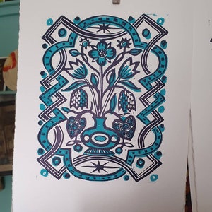 May include: A blue and black linocut print of a stylized floral arrangement in a vase. The vase is decorated with a geometric pattern and the flowers are stylized with a simple design.