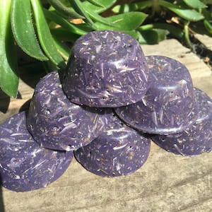 May include: A stack of five purple and white soap bars with a speckled appearance. The soap bars are arranged in a pyramid shape on a wooden surface.