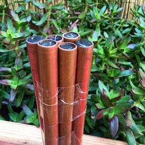 Peut inclure: Un groupe de six tuyaux en cuivre avec des bouchons noirs sont regroupés et fixés avec du ruban adhésif transparent. Les tuyaux sont disposés verticalement et sont posés sur une surface en bois.