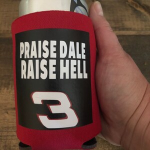 Puede incluir: Enfriador de latas rojo con texto en blanco y negro que dice "Praise Dale Raise Hell" y un n&uacute;mero blanco "3" sobre un fondo negro.
