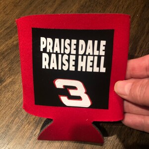 Puede incluir: Enfriador de latas rojo con un parche negro que muestra el texto "Praise Dale Raise Hell" y el n&uacute;mero "3" en blanco.
