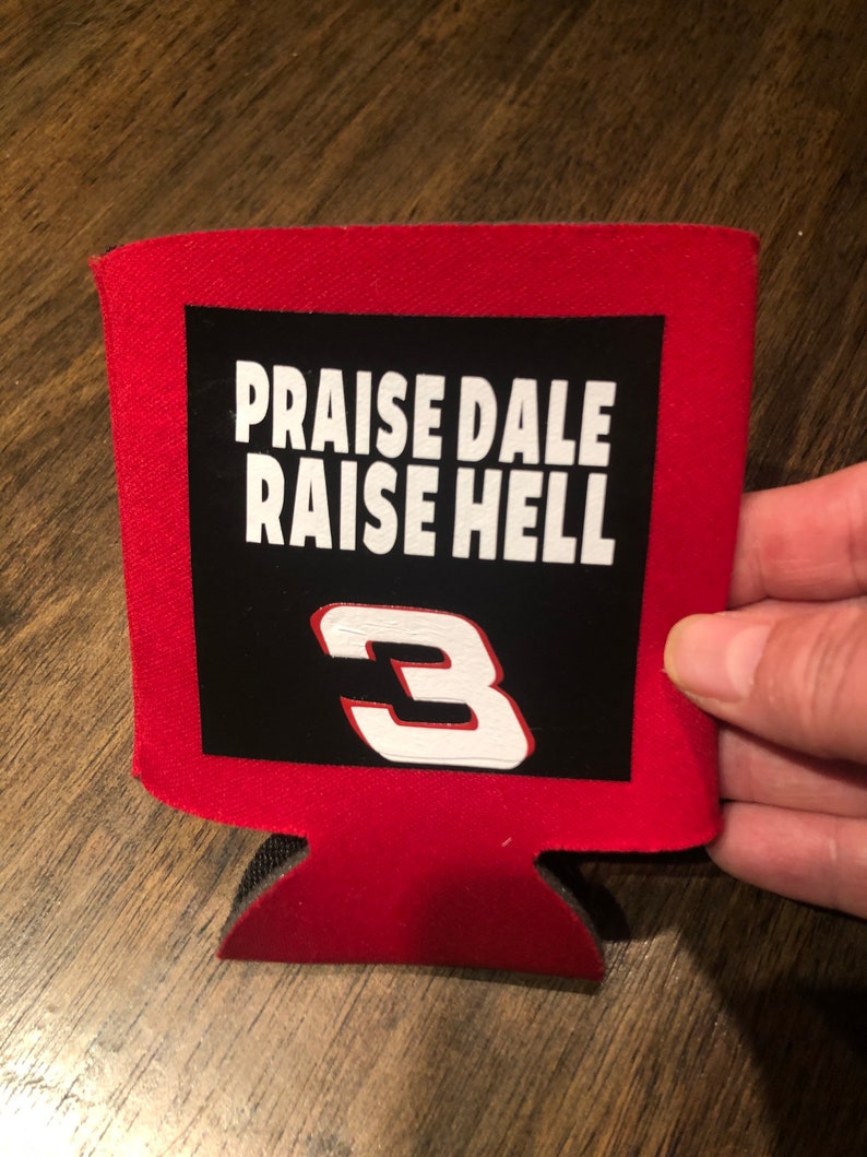 Puede incluir: Enfriador de latas rojo con un parche negro que muestra el texto "Praise Dale Raise Hell" y el n&uacute;mero "3" en blanco.