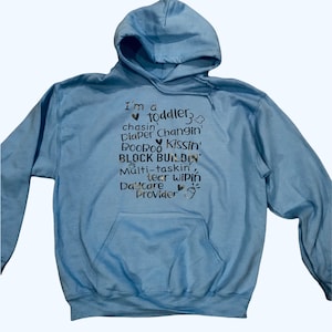 May include: A light blue hoodie with a white pocket and the text "I'm a toddler, chasin' changin' diaper, BOOBOO kissin', BLOCK BUILDIN', Multi-taskin', tear wipin', Daycare Provider" printed on the front.