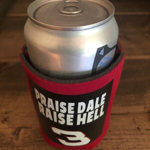 Puede incluir: Enfriador de latas rojo y negro con el texto "Praise Dale Raise Hell" y el n&uacute;mero "3" en blanco.