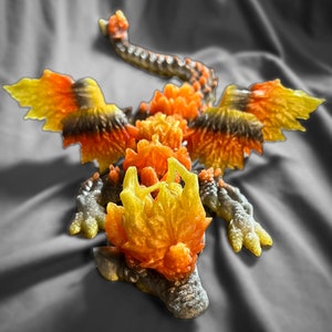 May include: A 3D printed dragon figurine with a yellow, orange, and black color scheme. The dragon has wings and a spiky head.
