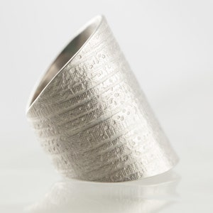 Peut inclure: Une bague en argent avec une surface textur&eacute;e et un motif. La bague est inclin&eacute;e et semble &ecirc;tre en m&eacute;tal.