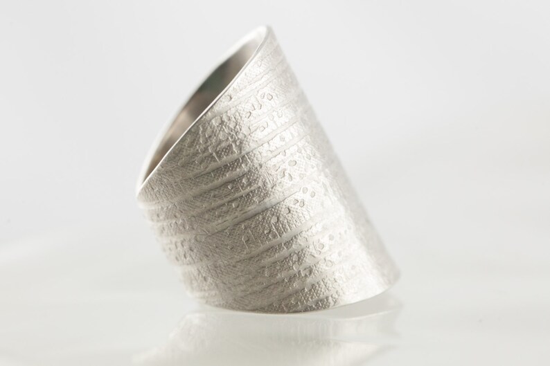Peut inclure: Une bague en argent avec une surface textur&eacute;e et un motif. La bague est inclin&eacute;e et semble &ecirc;tre en m&eacute;tal.
