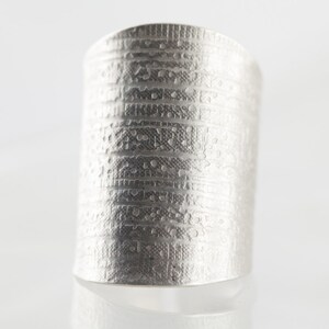 Peut inclure: Une bague en argent avec un motif textur&eacute; et un design. La bague est large et a un dessus plat.
