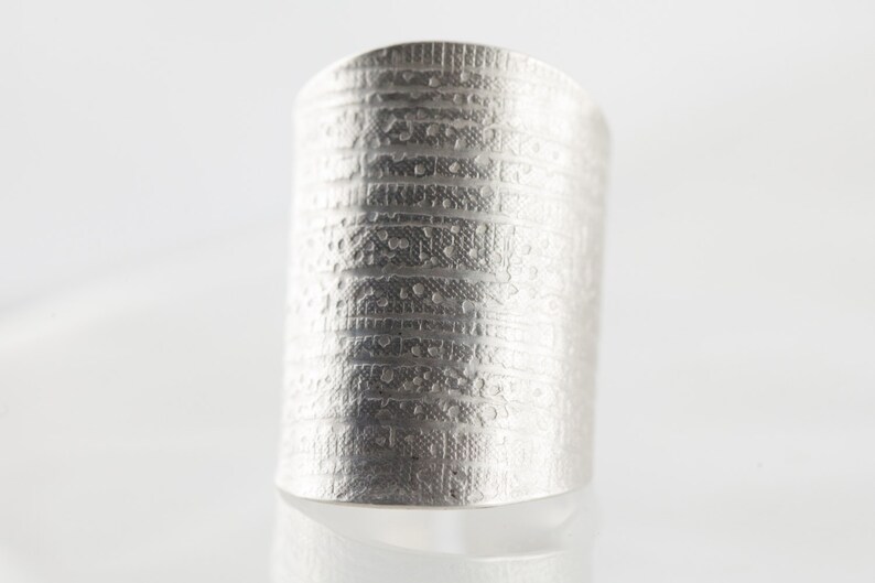 Peut inclure: Une bague en argent avec un motif textur&eacute; et un design. La bague est large et a un dessus plat.