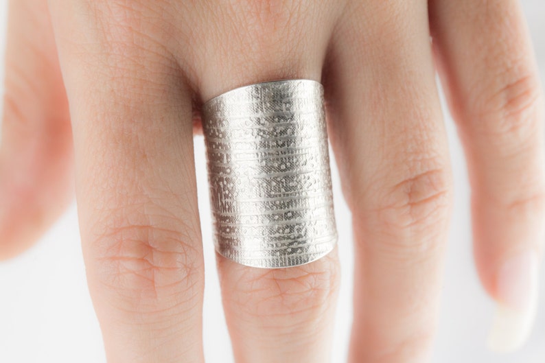 Peut inclure: Une bague en argent avec une surface textur&eacute;e. La bague est large et de forme cylindrique.