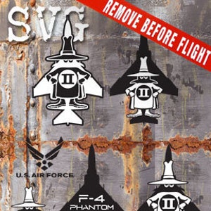May include: Black and white silhouette of a cartoon character wearing a hat and cape, with the text "II" on the chest. The character is standing in front of a jet fighter plane. The text "REMOVE BEFORE FLIGHT" is written in white letters on a red background at the top of the image. The text "U.S. AIR FORCE" is written in white letters on a blue background at the bottom of the image. The text "F-4 PHANTOM II" is written in white letters on a black background below the character.