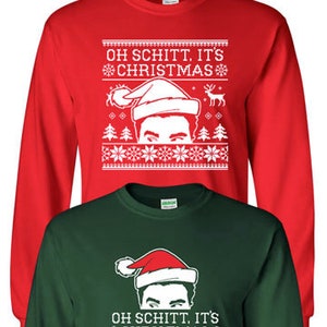 Puede incluir: Dos camisas de manga larga con temática navideña. La camisa roja presenta un diseño blanco con el texto "Oh Schitt, It's Christmas" y una imagen de dibujos animados de un hombre con un gorro de Papá Noel. La camisa verde presenta el mismo texto e imagen en blanco.