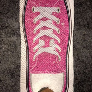 May include: A pink and white patterned sock shaped like a sneaker. The sock has a hole in the toe area.