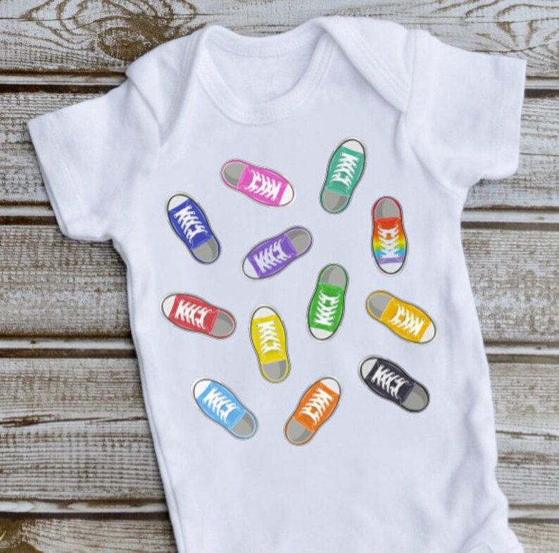 May include: White baby onesie with a colorful print of various sneakers. The sneakers are in different colors, including red, blue, green, yellow, and purple.