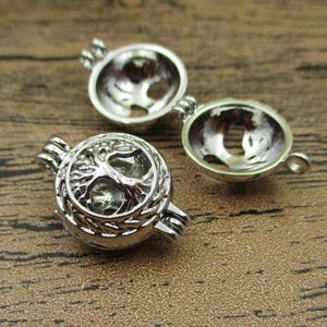 Pode incluir: Dois pingentes de prata com design de árvore. Os pingentes são abertos e têm um pequeno laço na parte superior para prender a uma corrente.