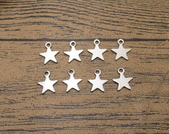Puede incluir: Ocho abalorios de estrella plateados con un bucle en la parte superior, dispuestos en dos filas sobre una superficie de madera marrón.