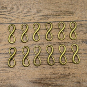 Peut inclure: Douze breloques en forme d'infini de couleur or antique. Les breloques sont disposées en deux rangées de six sur une surface en bois.