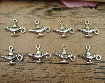 Op de afbeelding: Tien zilverkleurige metalen bedels in de vorm van Aladdin's magische lamp. Elke bedel heeft ingewikkelde details en een lus om aan een ketting of armband te bevestigen.
