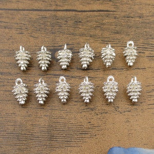 Può includere: Dodici ciondoli a forma di pigna argentati con un anello nella parte superiore per attaccarli a gioielli o altri oggetti artigianali.