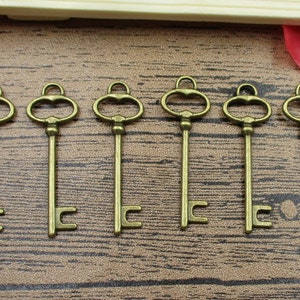 Pode incluir: Seis chaves esqueleto de tom dourado antigo com buracos de fechadura ornamentados. As chaves estão dispostas em fila sobre uma superfície de madeira.